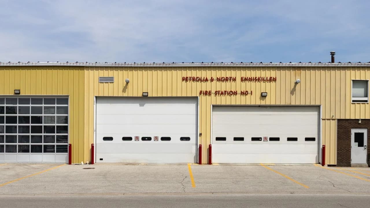 Exterior of a single-storey yellow fire station with four equipment bays under a blue sky; no people visible.