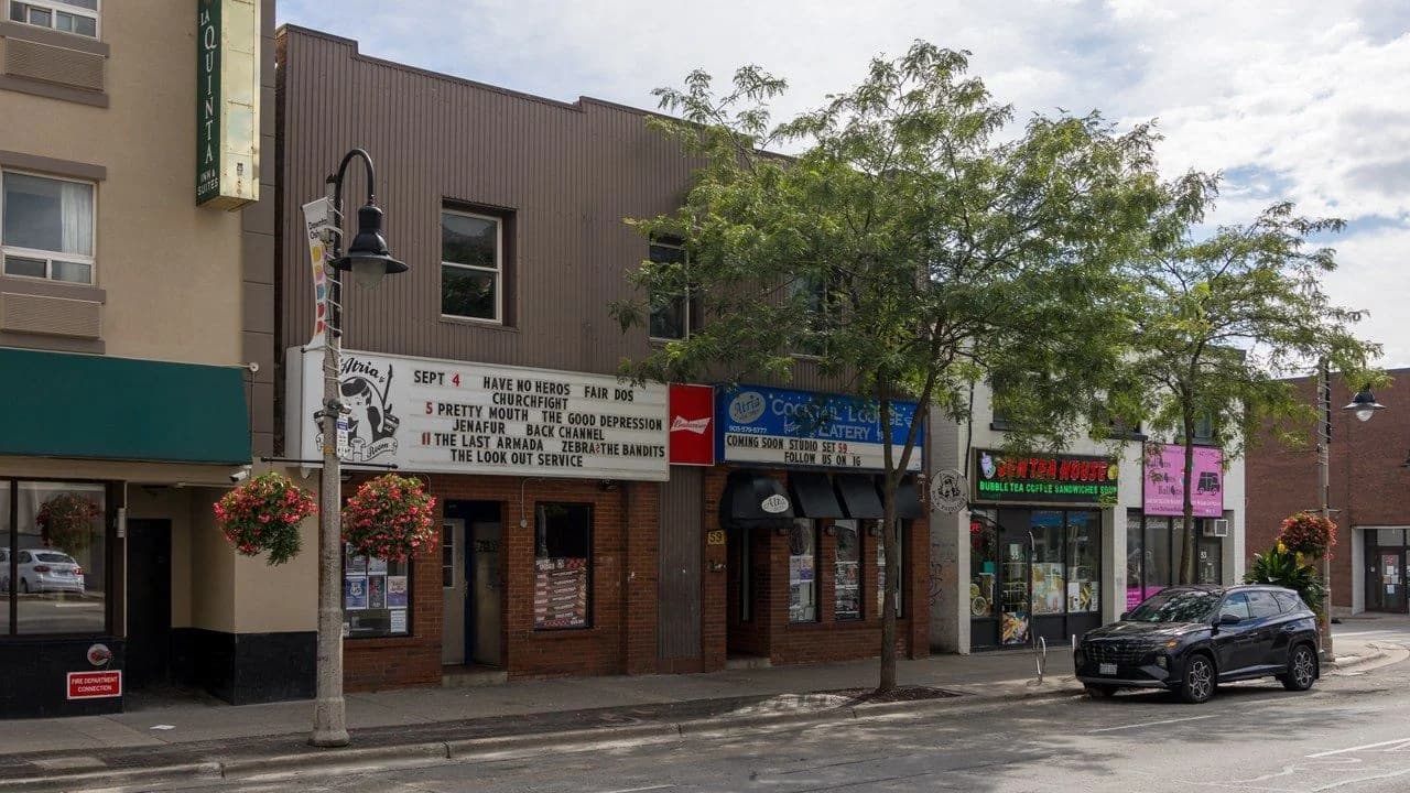 Downtown Oshawa streetscape with storefronts, trees and a parked vehicle; no people visible
