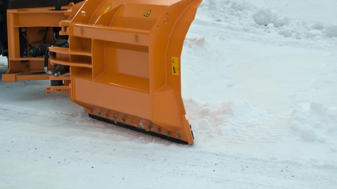 Orange snowplow blade clearing snow; no people visible.