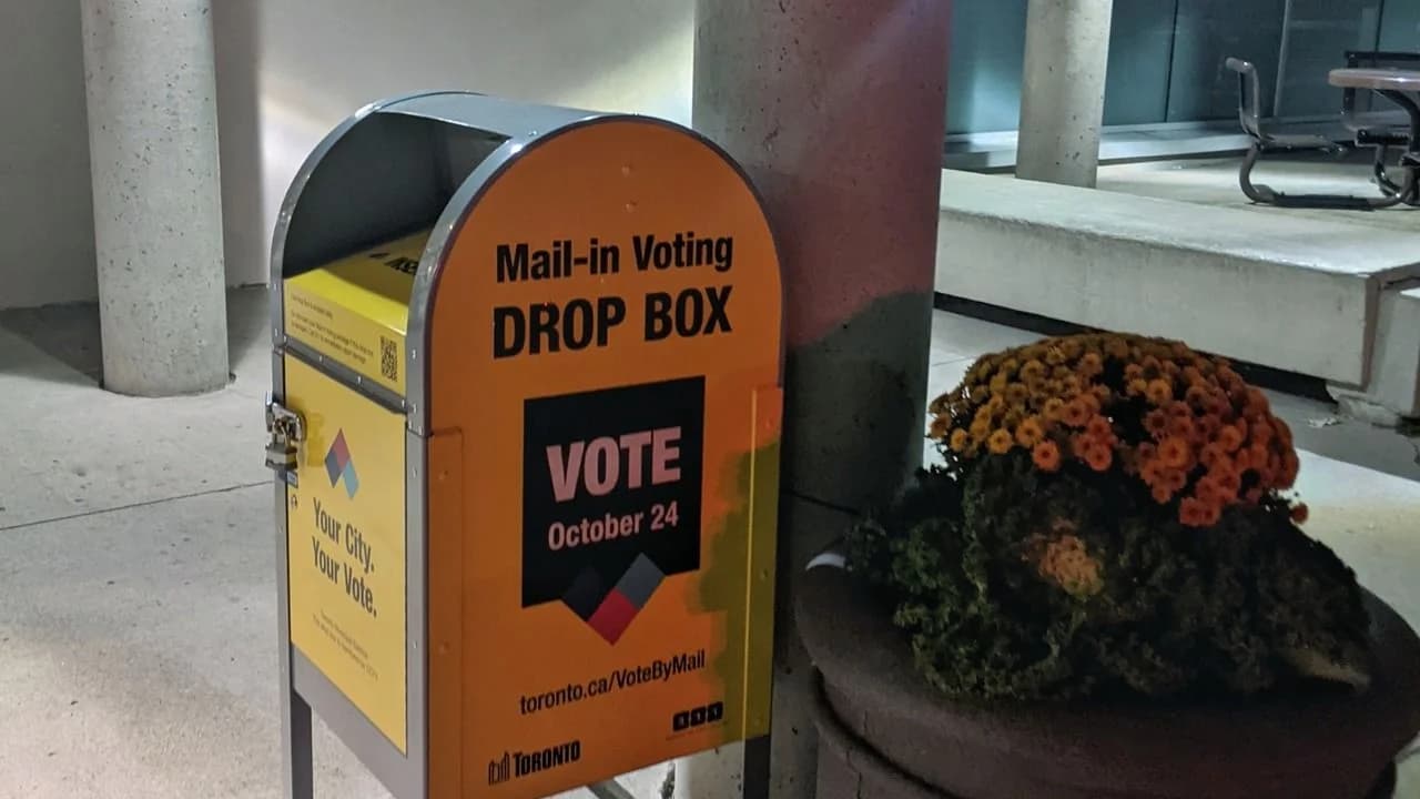 A mail-in voting drop box marked VOTE outside a community building at night; no people visible.