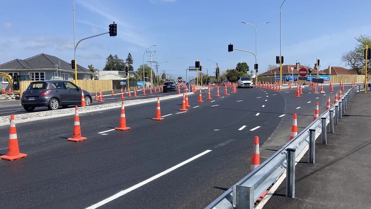 A newly paved road intersection with rows of orange traffic cones marking construction zones; no people visible.