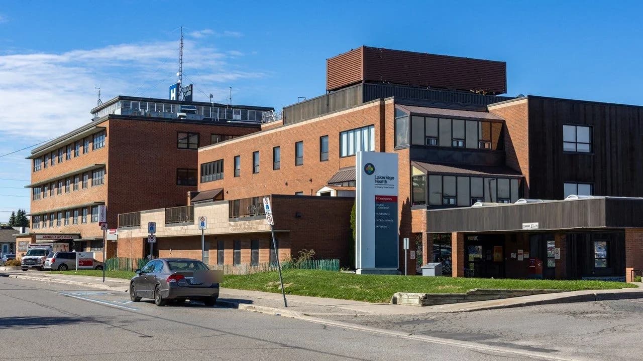 Brick exterior of Lakeridge Health Bowmanville hospital with wayfinding sign, emergency ambulance bay and main entrance; no people.