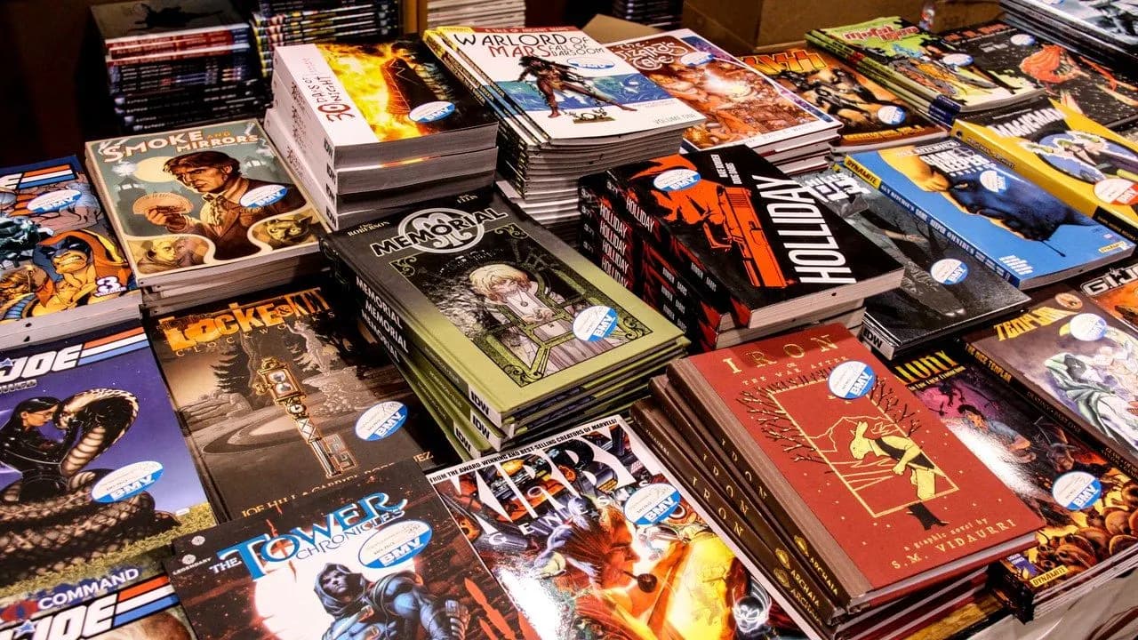 Stacks of colourful comic books on a table at a convention; no people visible