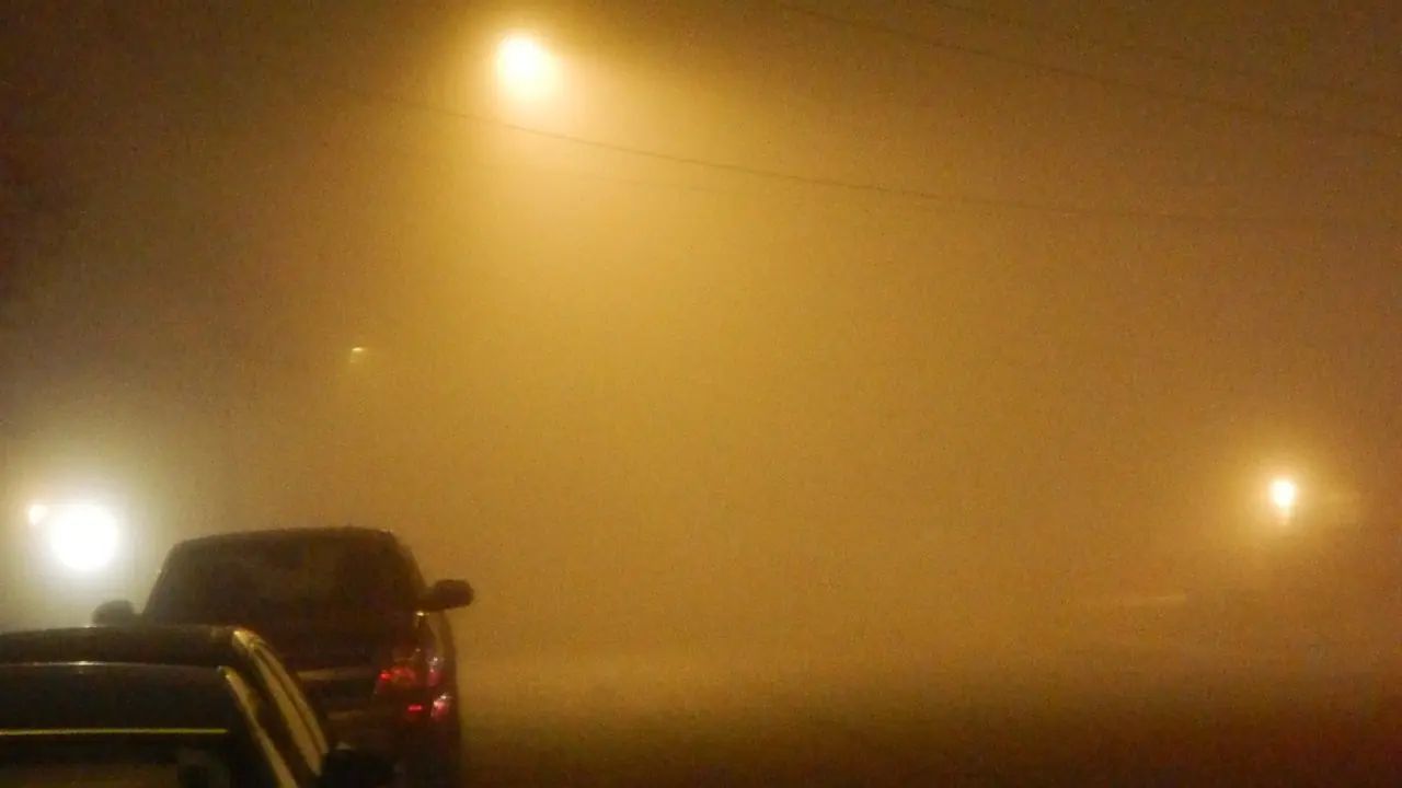 Streetlights glowing through fog on a residential street at night, with car headlights visible; no people in frame.