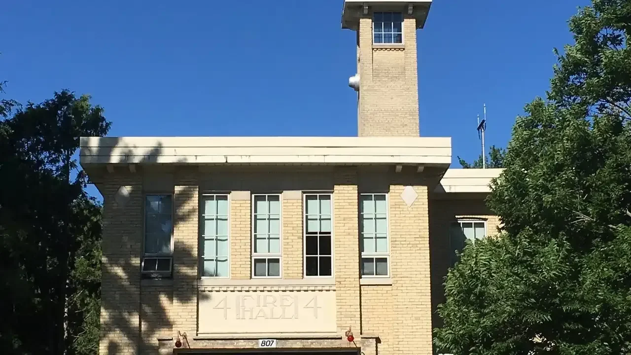 Historic brick fire hall with a hose tower and carved 'Fire Hall 4' stone signage under a blue sky.