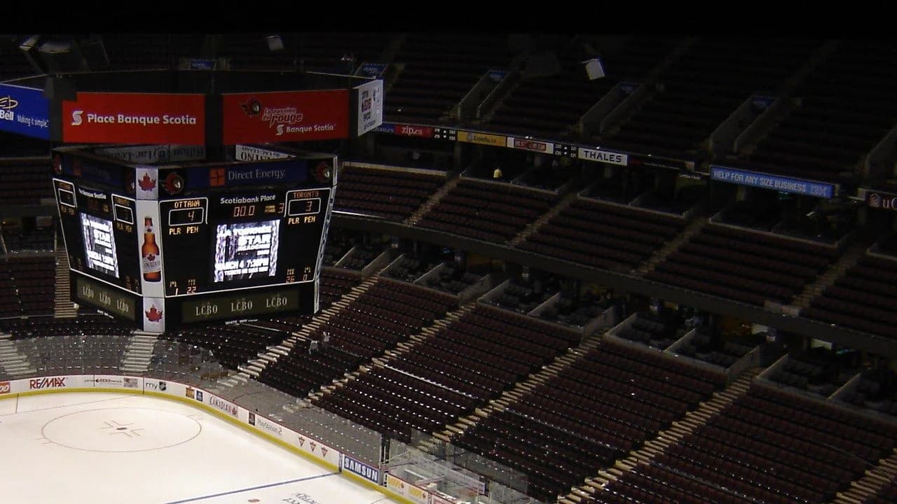Empty hockey arena interior with a pristine ice surface, jumbotron and rows of vacant seats; no people visible.