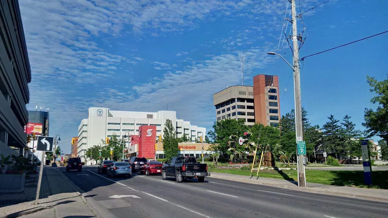 Daytime streetscape of downtown Oshawa on King Street with commercial buildings, parked cars and moving traffic; no people visible