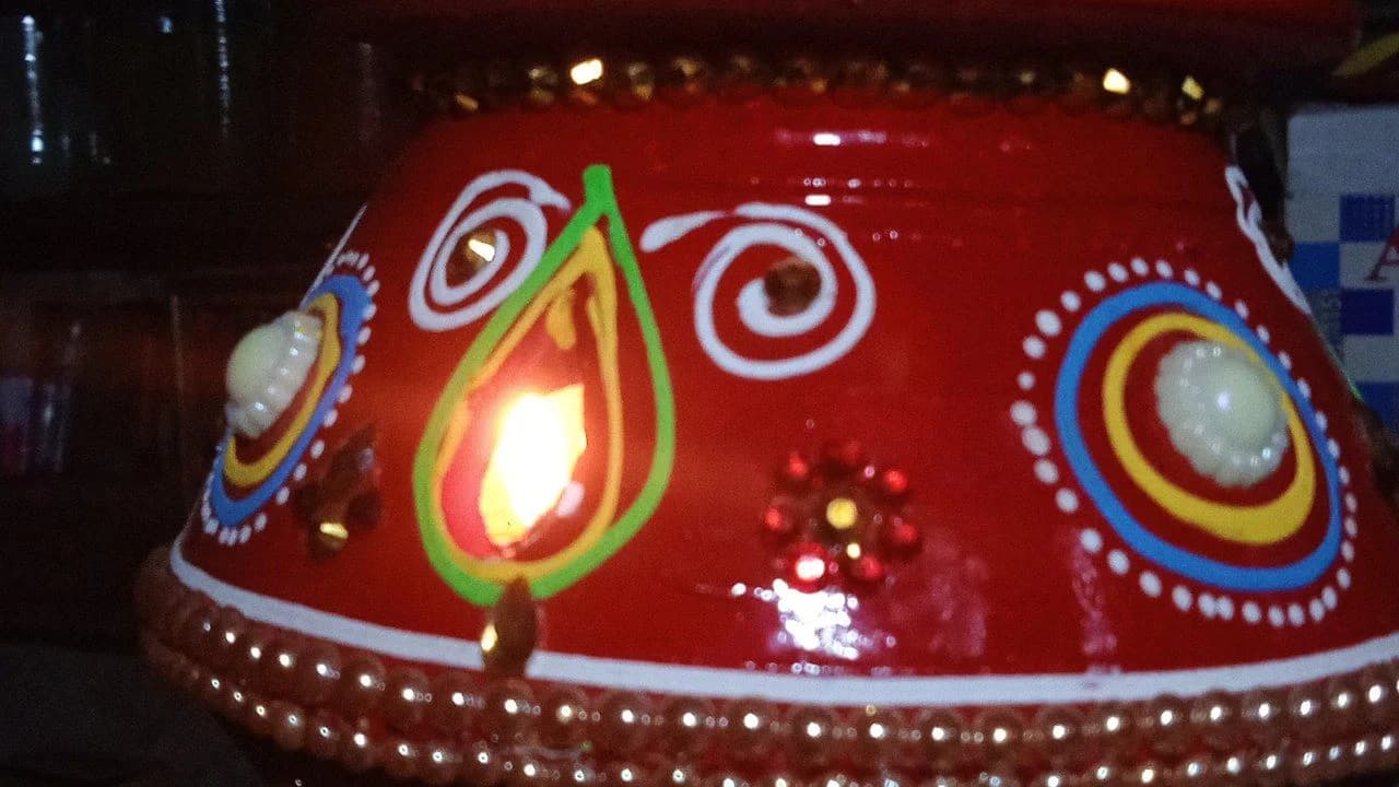Close-up of a decorated red earthen garbo pot with a lit diya, used during Navratri and Garba celebrations; no people visible.
